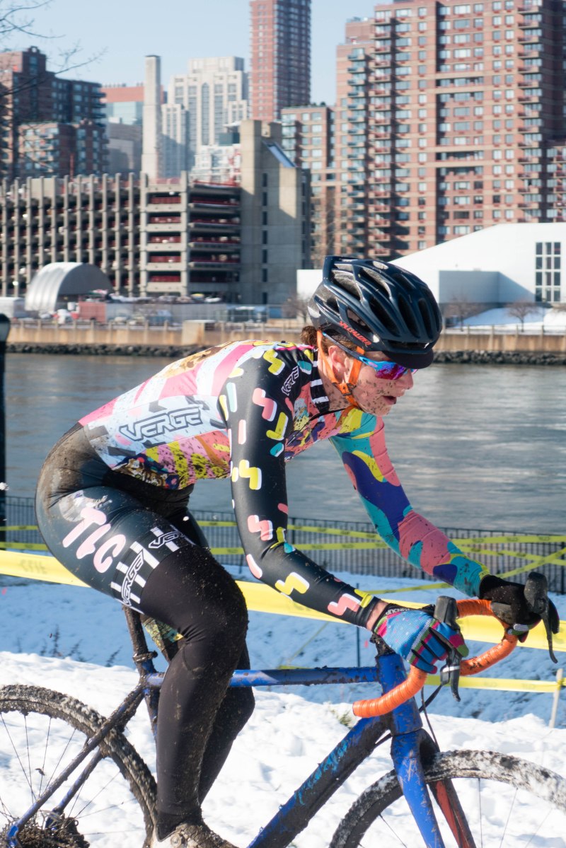 woman races cyclocross in mud, snow, New York City background